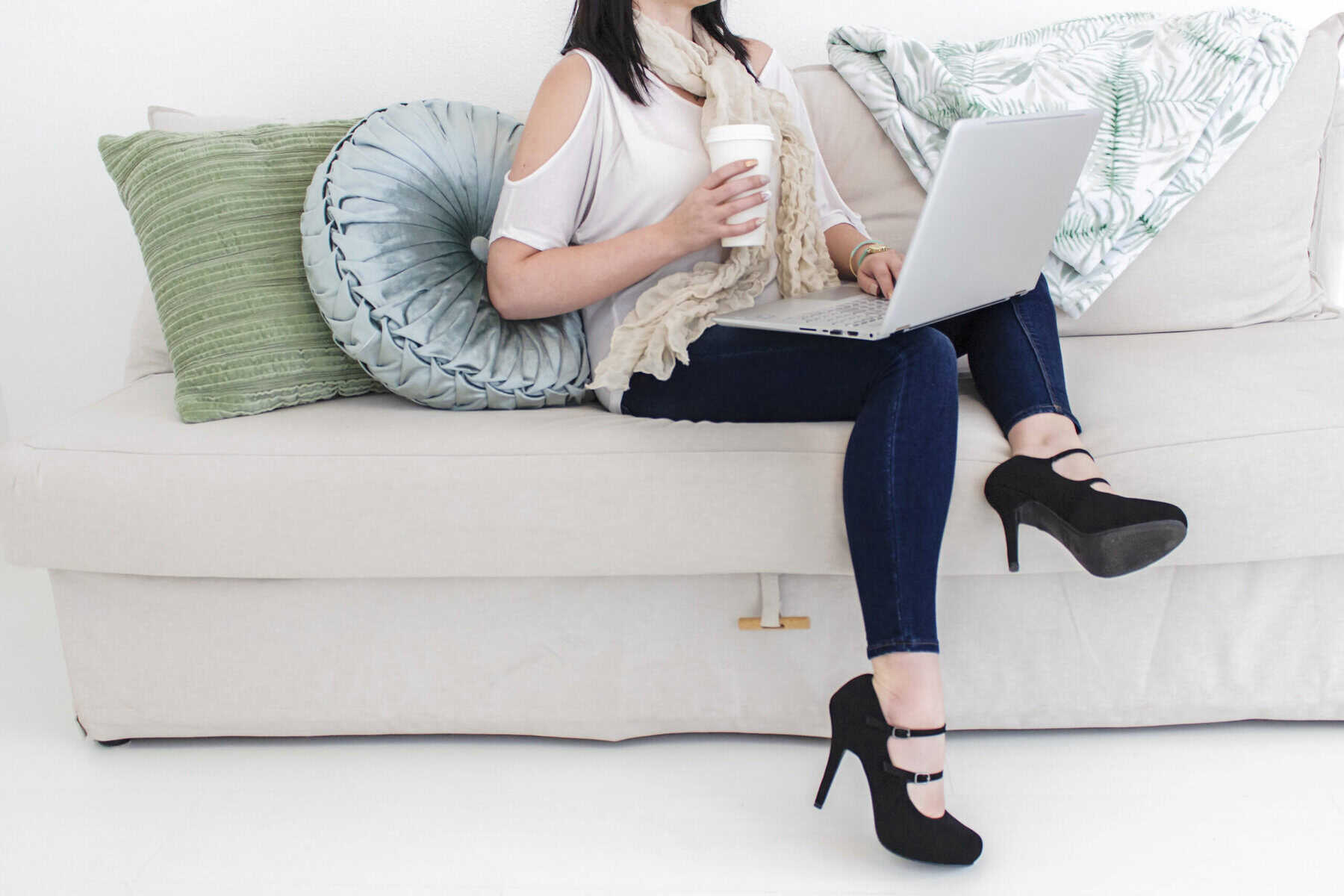Woman sitting on the couch working on her laptop with a cup of coffee in her hand.