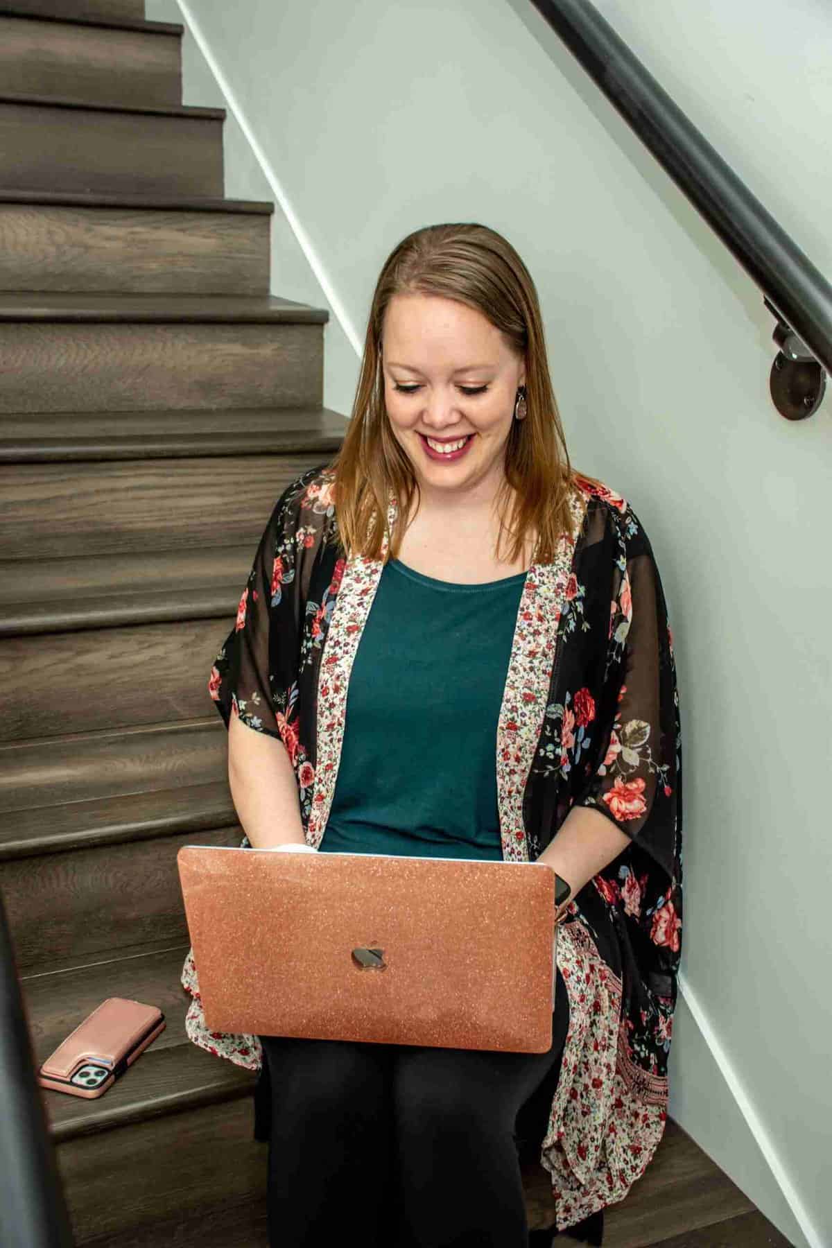 Black Friday Sale 4 Melissa Mackey, brand strategy and web design services for ADHD entrepreneurs, sitting on some stairs smiling at her computer that is in her lap