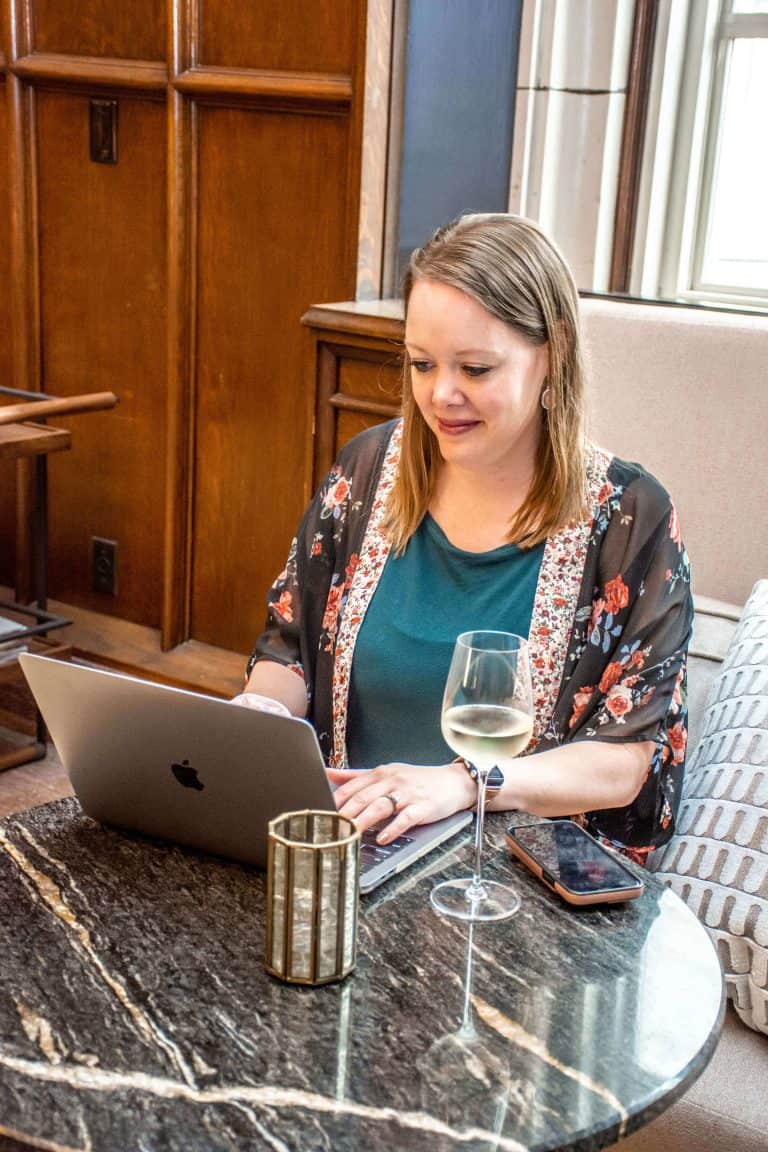 Black Friday Sale 3 Melissa Mackey, branding and web design for ADHD entrepreneurs, looking down at her computer as she works with a glass of wine on the table beside her