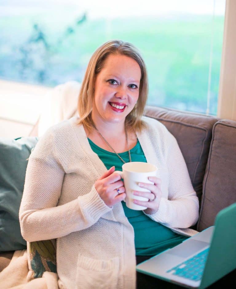 Melissa Mackey, web designer and messaging strategist for coaches and consultants. Melissa is sitting on sofa with a coffee mug wearing a white sweater and green shirt