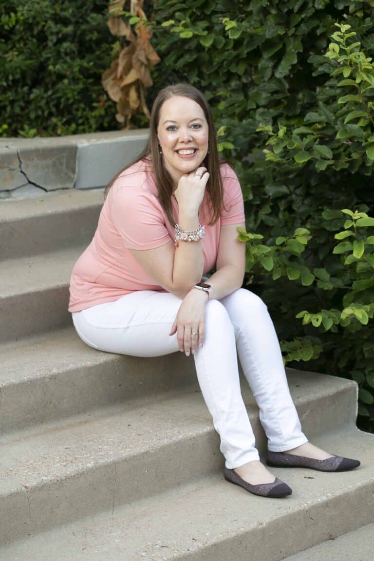 Melissa Mackey, web designer and messaging strategist for coaches and consultants, sitting outdoors on some stairs, smiling at the camera, wearing a light coral shirt
