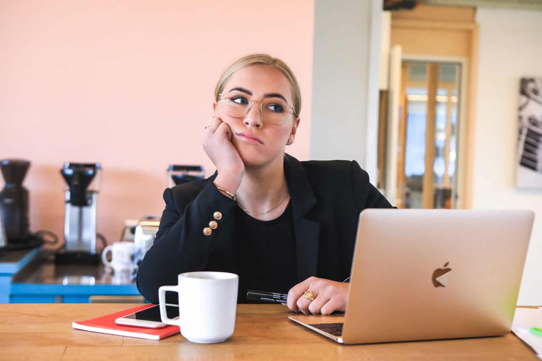 Woman sitting at a desk with her laptop, coffee, and notebook looking discouraged