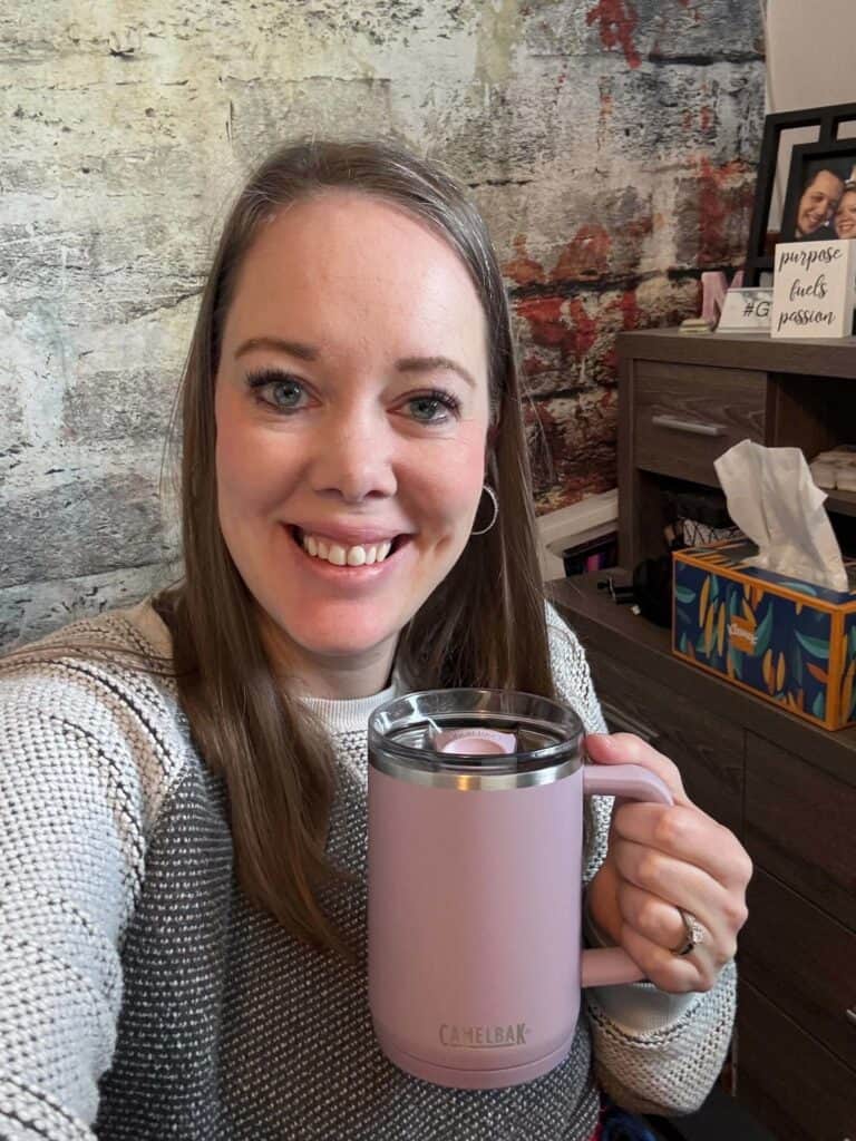 Melissa, millennial UGC creator, is smiling at the camera, holding up a light purple coffee mug